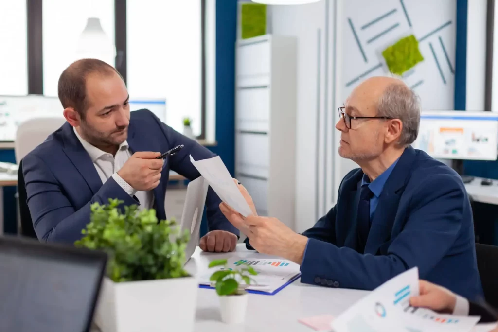 senior-entrepreneur-discussing-with-coworker-holding-documents-conference-briefing-businessman-discussing-ideas-with-colleagues-about-financial-strategy-new-start-up-company-1-scaled